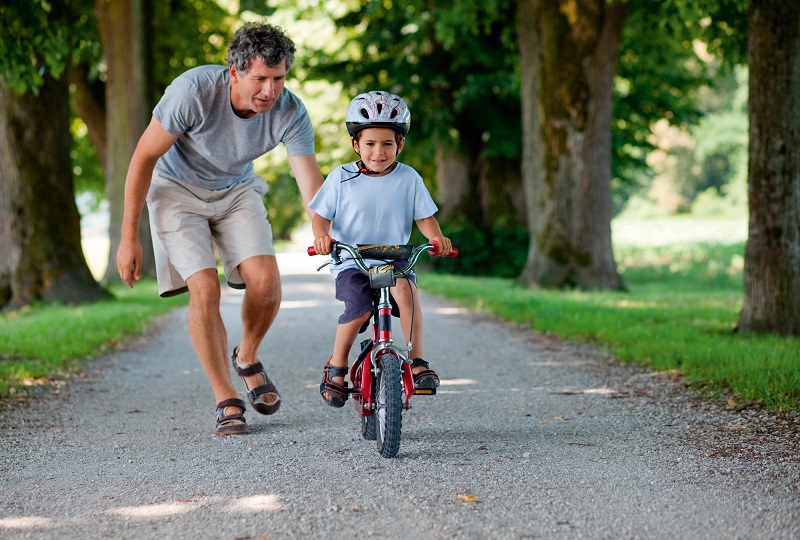 папа учит ребенка кататься на велосипеде